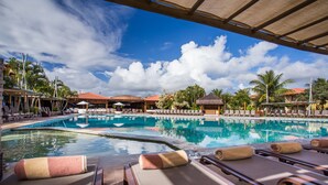 A pool area with lounge chairs and umbrellas, surrounded by palm trees and buildings with red roofs. - La Torre Resort All Inclusive (Porto Seguro)