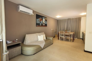 A modern living room with a sofa, a painting, a dining table with chairs, and an air conditioning unit.
