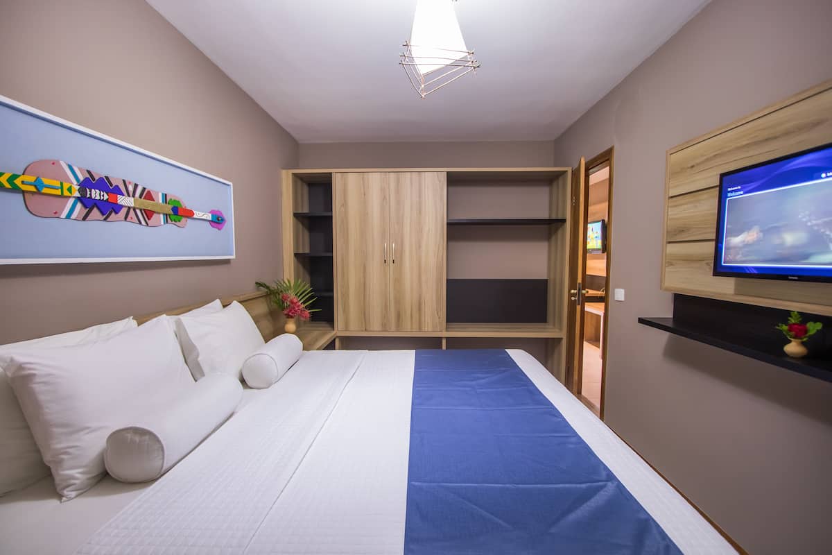 A modern hotel room with a bed, a TV, a wardrobe, and a painting on the wall.