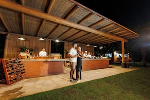 An outdoor bar area with a wooden ceiling, a counter with a wine rack, and a seating area. - La Torre Resort All Inclusive (Porto Seguro)