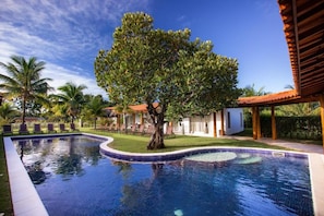 A swimming pool with a tiled edge, surrounded by lounge chairs and a tree. - La Torre Resort All Inclusive (Porto Seguro)