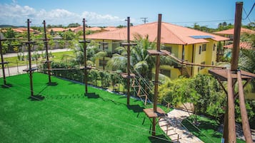 A residential area with a green lawn, wooden play structures, and houses with red-tiled roofs.