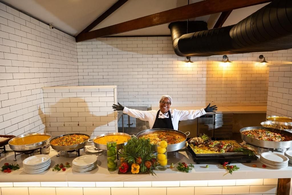 Disposição de buffet com diversos pratos e uma pessoa atrás do balcão.
