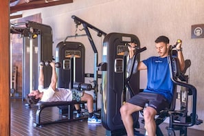 Two individuals using gym equipment in a fitness area with a bench and weight machines.