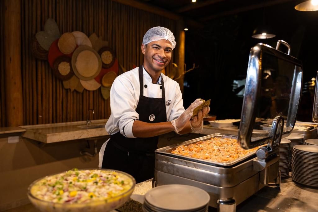 Disposição de buffet com um chefe servindo comida, um grande recipiente de metal e uma pizza em uma tigela.