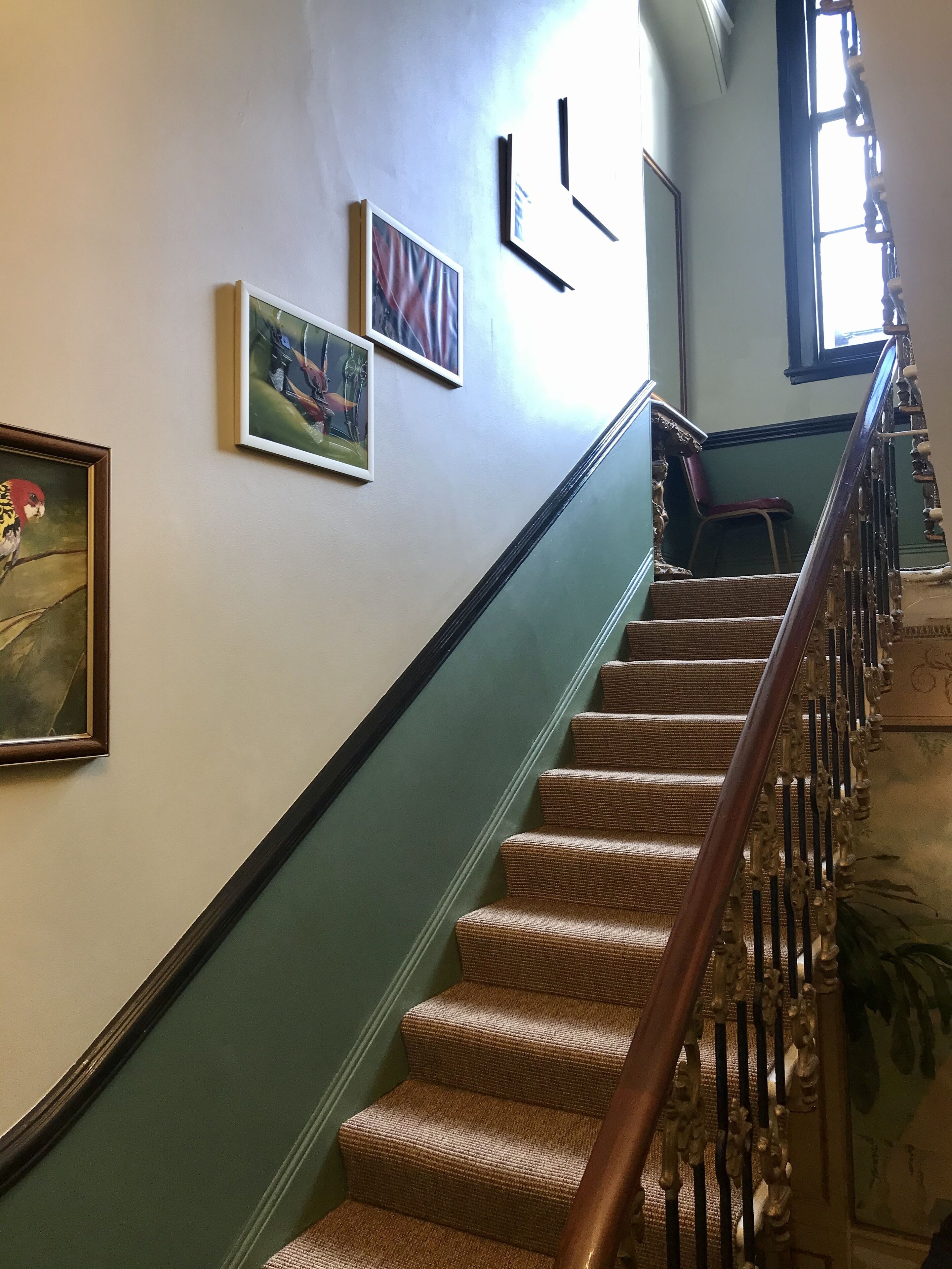 A staircase with a wooden handrail and carpeted steps, leading to a landing with a chair and a window.