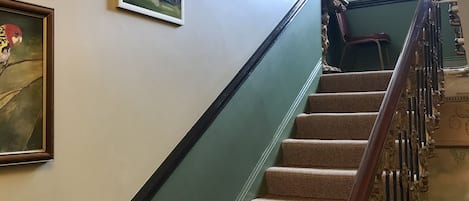 A staircase with a wooden handrail and carpeted steps, leading to a landing with a chair and a window.