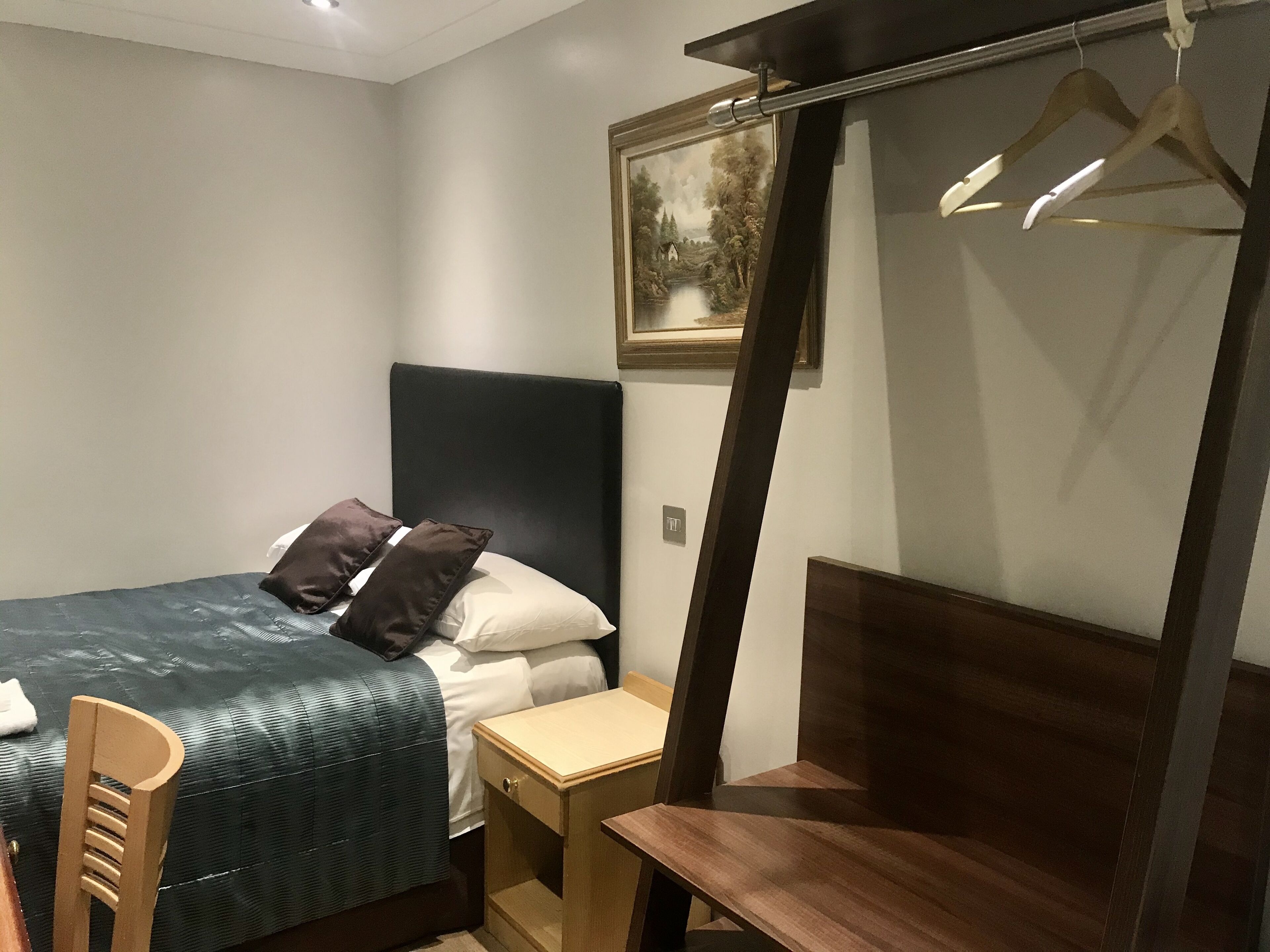 A neatly arranged bedroom with a bed, bedside table, chair, and a hanging clothes rack.