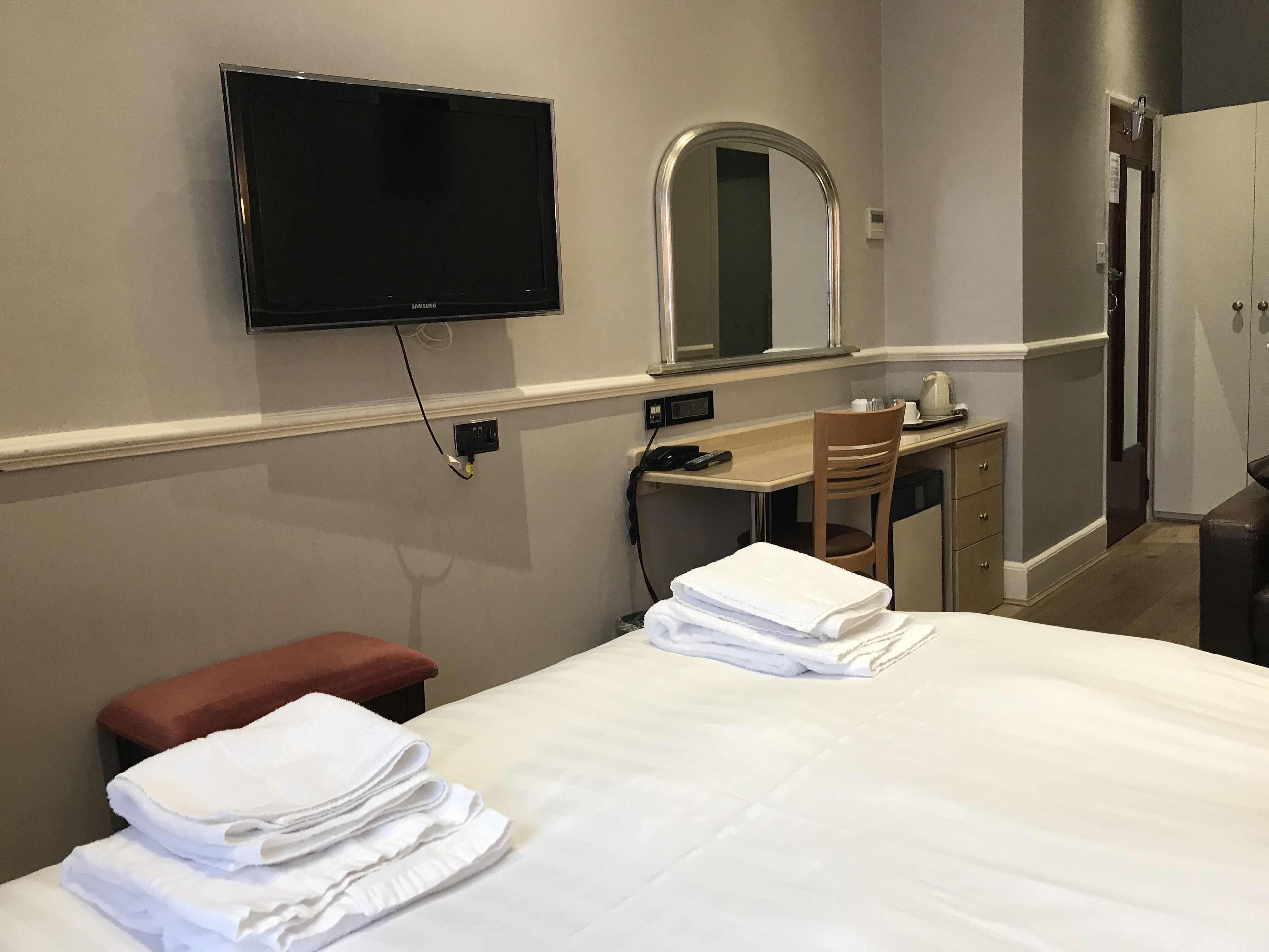 Een hotelkamer met een bed, een bureau, een stoel, een aan de muur bevestigde televisie en een spiegel.