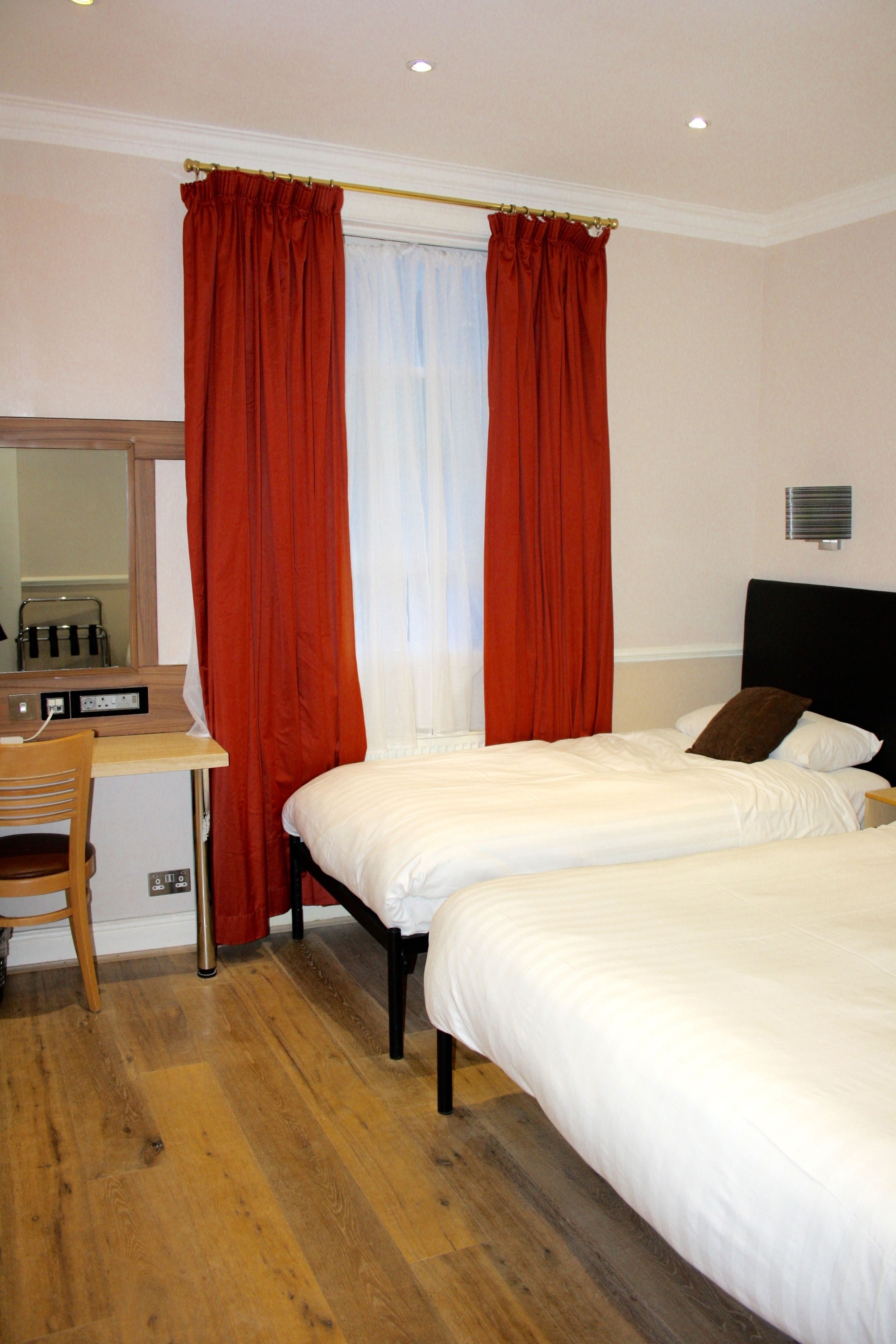 A hotel room with two beds, a desk, and a mirror.
