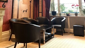 A room with a large window, two black leather chairs, a small table, and a radiator.