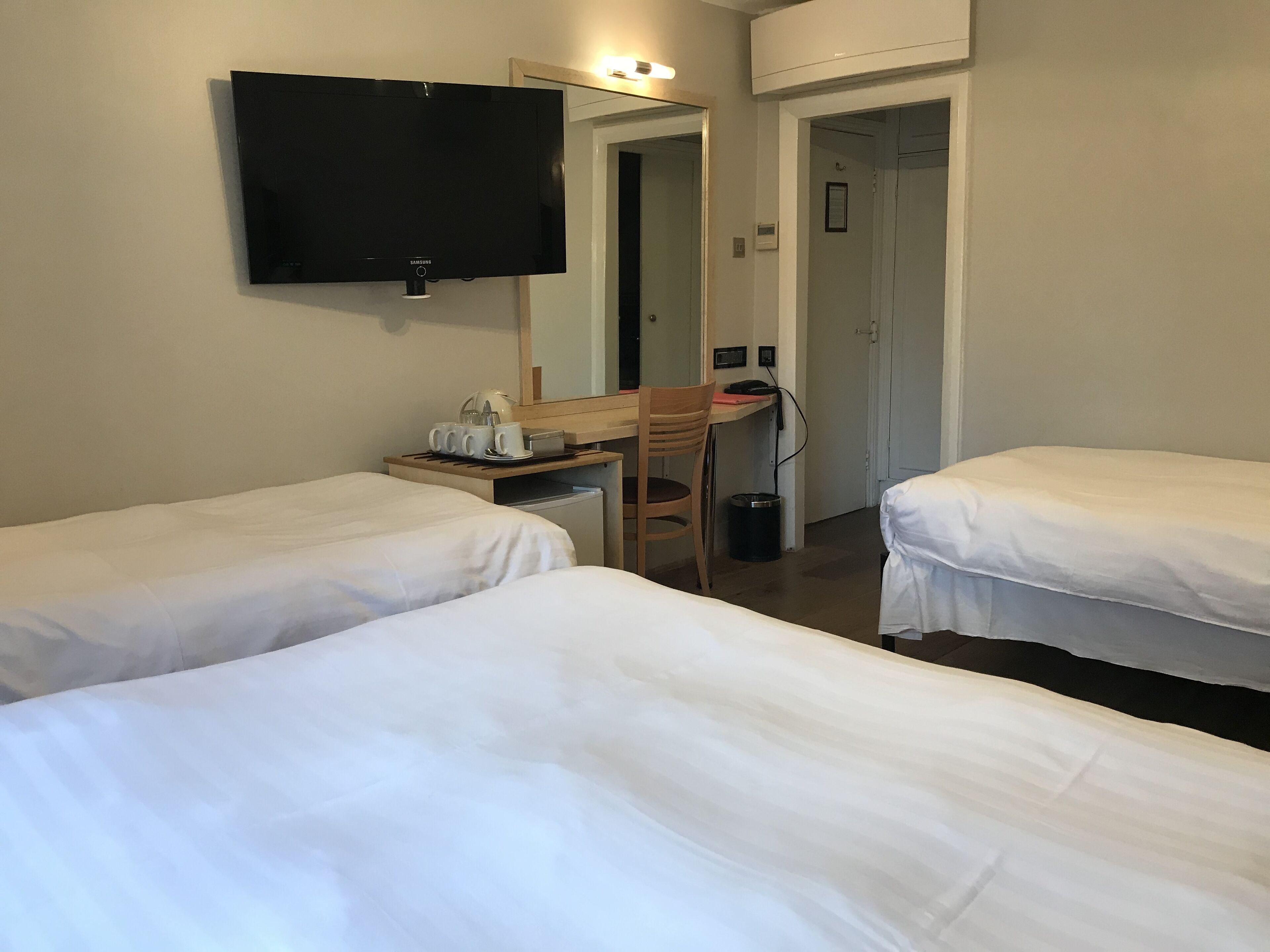 Une chambre d’hôtel avec deux lits simples, un bureau avec une chaise, une télévision et une petite poubelle.