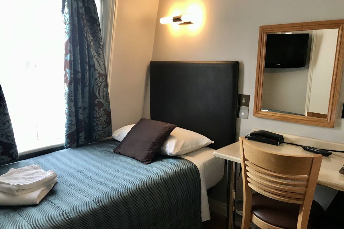 Une chambre d’hôtel équipée d’un lit, d’un bureau, d’une chaise, d’une télévision et d’une fenêtre avec des rideaux.