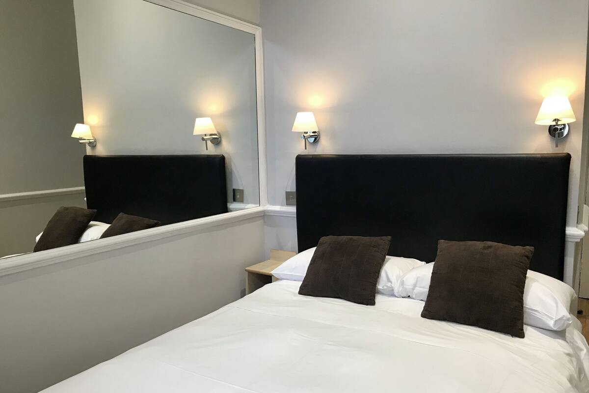 Une chambre d’hôtel avec un grand lit, deux tables de chevet et des lampes fixées au mur.