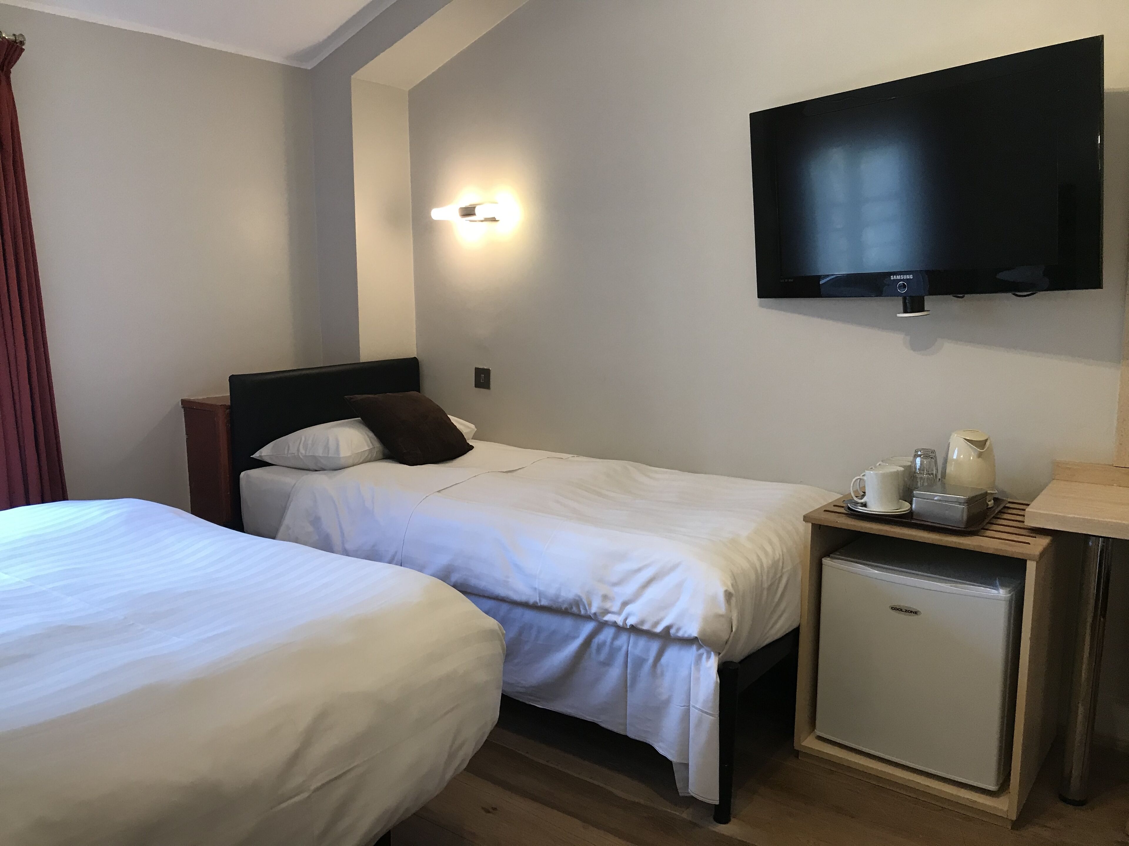 Une chambre d’hôtel avec deux lits, une télévision, un petit réfrigérateur et une table de chevet avec une bouilloire et des tasses.
