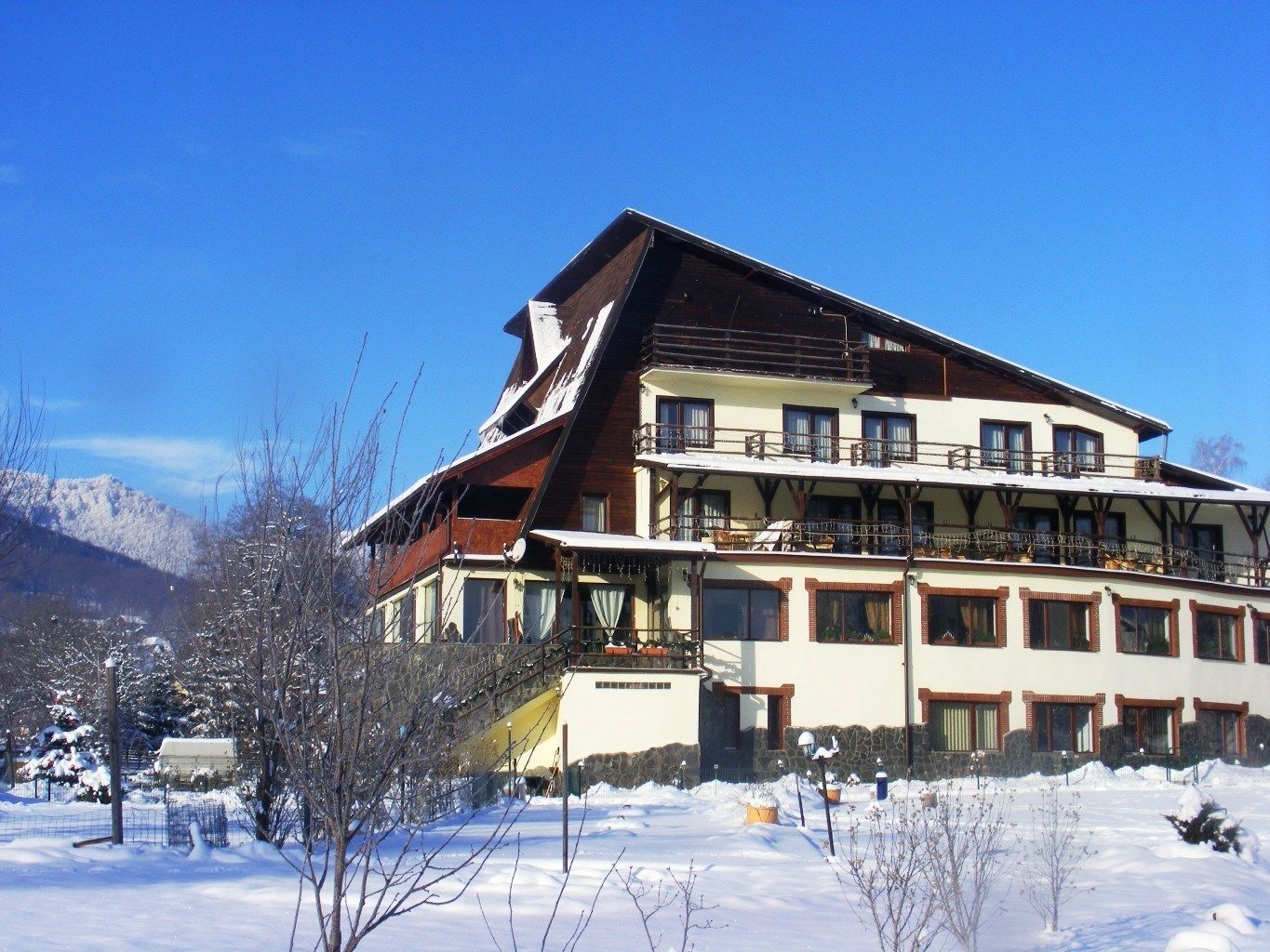 Un hotel de varios pisos con techo inclinado, balcones y vistas a montañas nevadas.