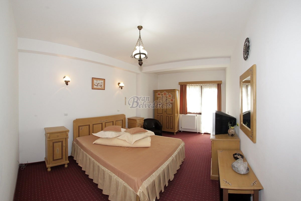 Une chambre à coucher comprenant un lit, des tables de chevet, une armoire, un bureau, une chaise, un miroir et un lustre.