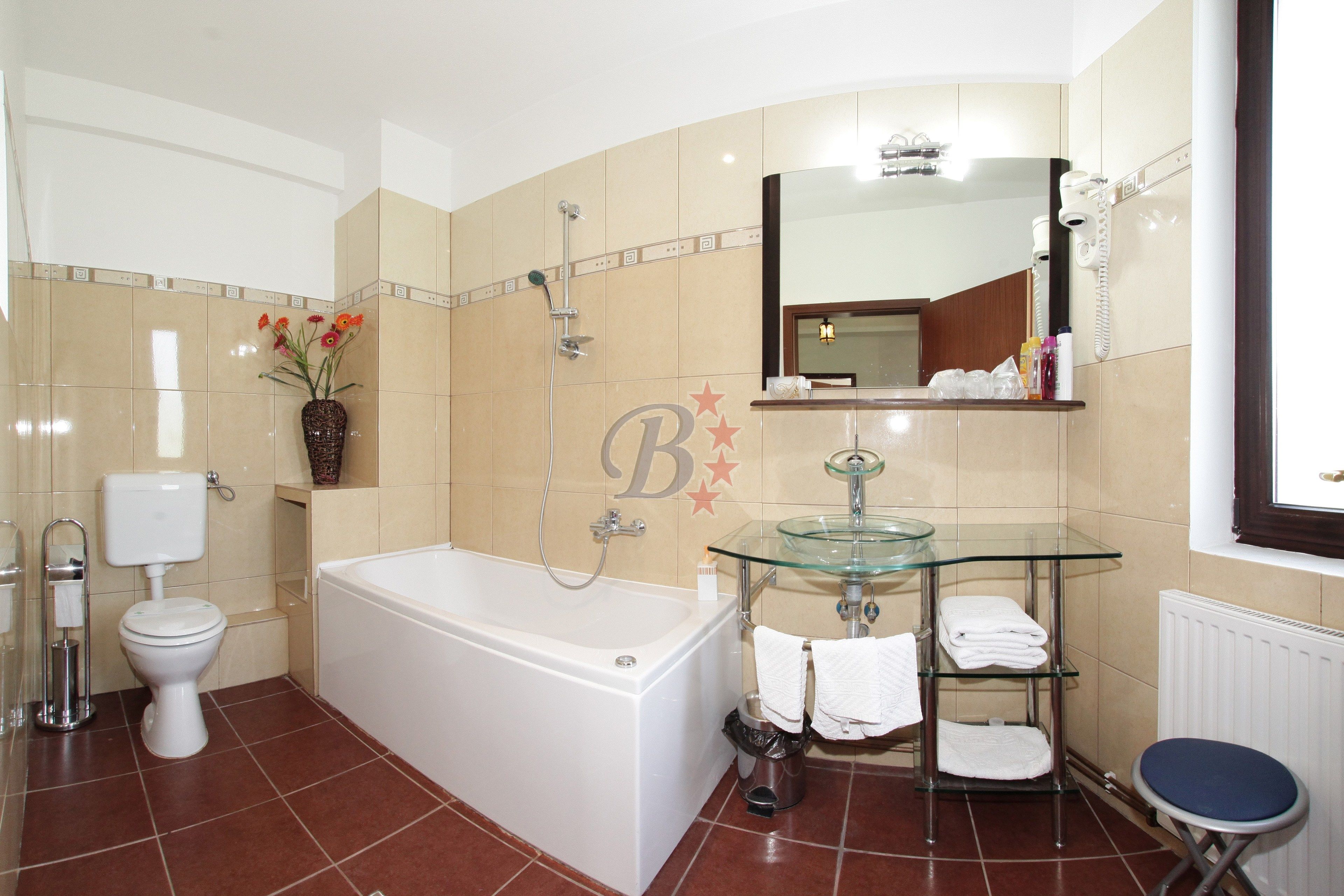 A bathroom with a bathtub, toilet, glass sink, and a mirror above the sink.