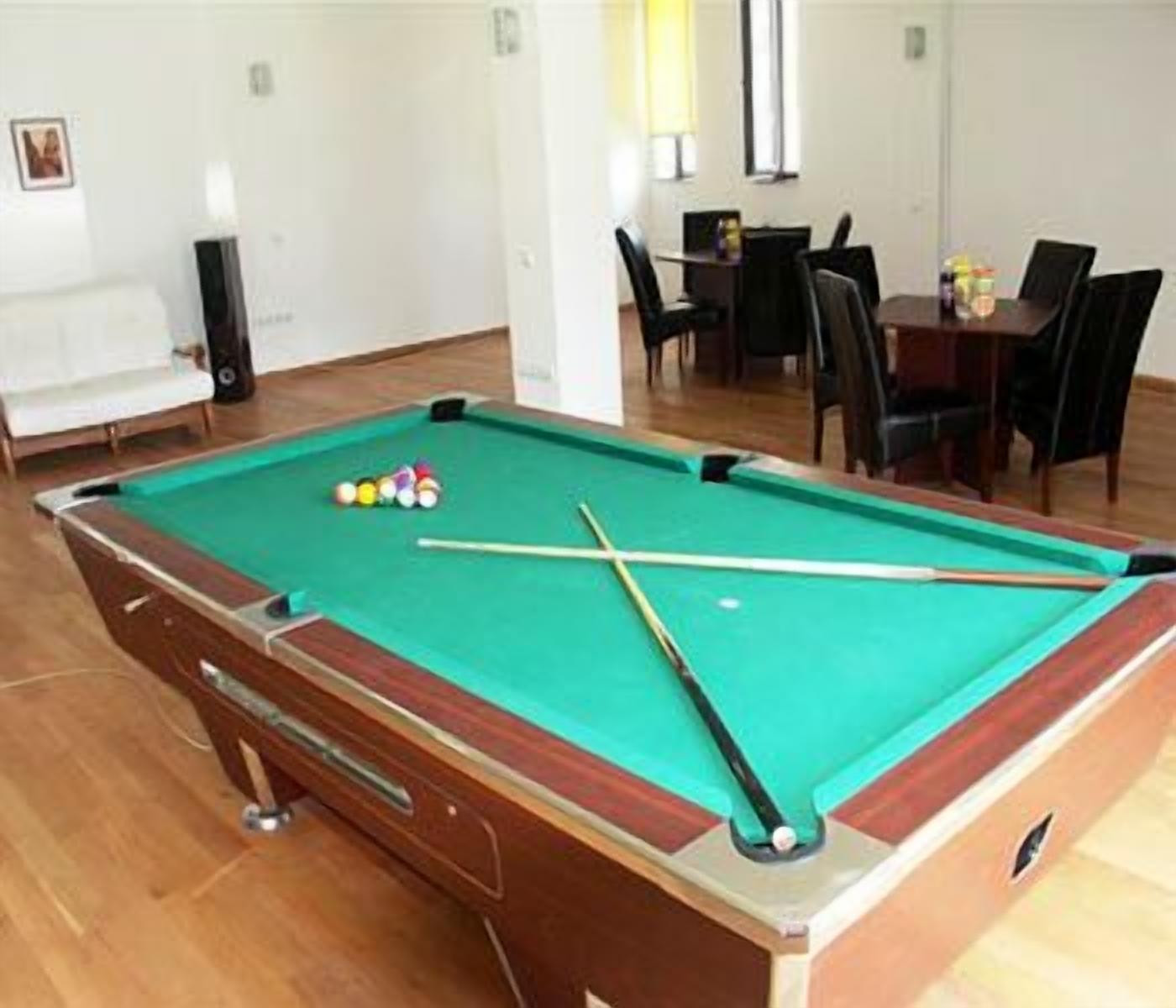 A pool table with balls and cues, a sofa, and a dining area with chairs and a table.