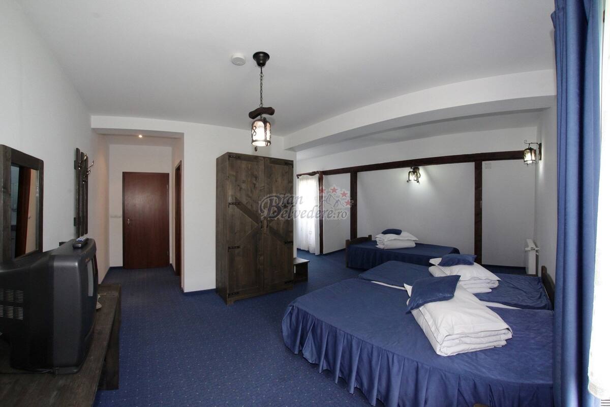 Une chambre d’hôtel avec deux lits, une armoire en bois, un téléviseur et un ventilateur de plafond.