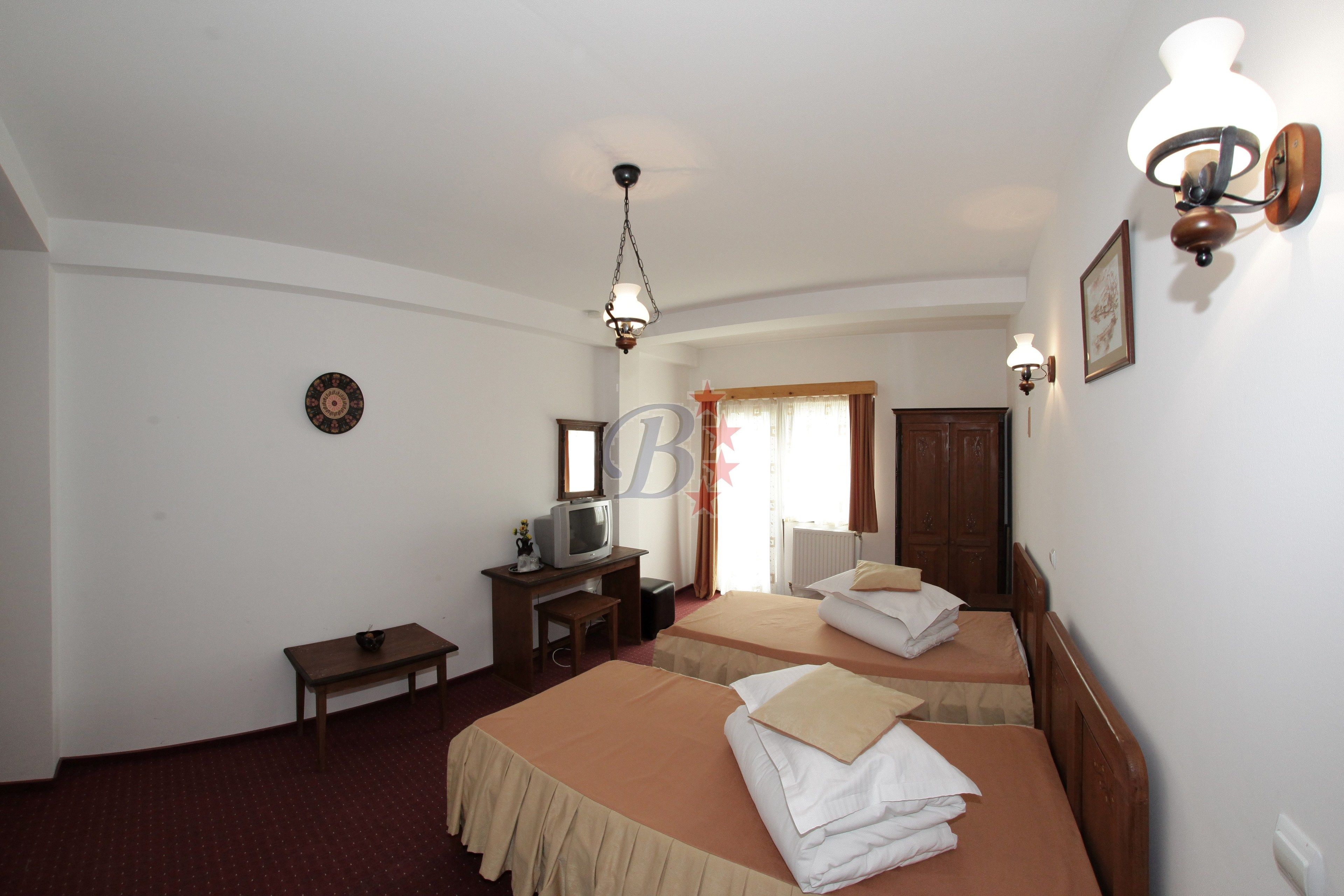 A hotel room with two beds, a desk with a television, a small table, and a lamp.