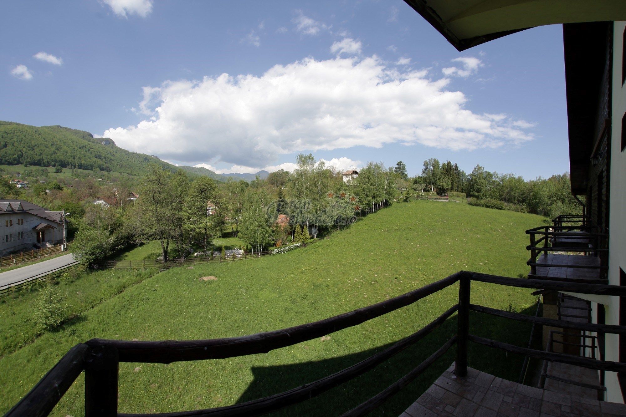 A balcony with a view of a green field, trees, and a mountain in the background.