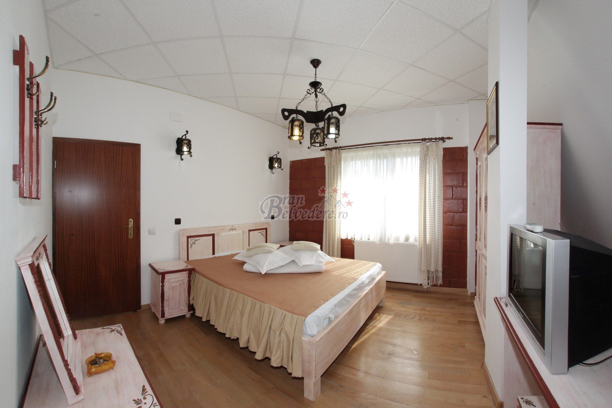 Quarto com cama, televisão, guarda-roupa e lustre.