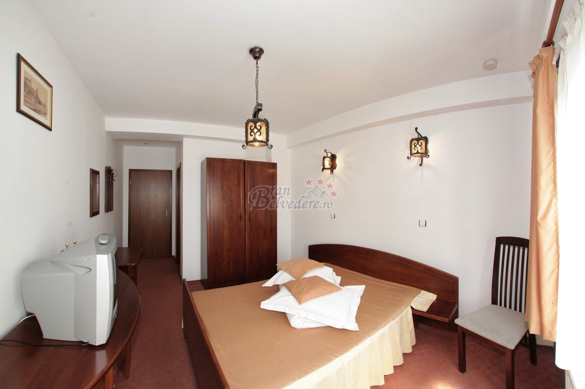 Habitación de hotel con cama, mesita de noche, lámpara y vista al pasillo.