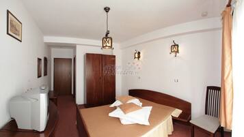 Habitación de hotel con cama, mesita de noche, lámpara y vista al pasillo.