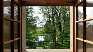 Une vue à travers une fenêtre à cadre en bois, dévoilant un paysage verdoyant et luxuriant avec un étang et des arbres.
