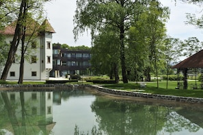 Ein friedlicher Park mit Teich, Laube und modernen Gebäuden im Hintergrund.