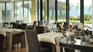 Une salle à manger avec des tables dressées pour un repas, un grand saladier en argent contenant des bouteilles de champagne, et une vue sur un paysage montagneux par de grandes fenêtres.