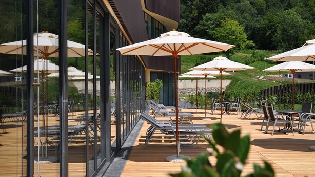 Un espace extérieur aménagé avec des chaises longues et des parasols, un mur de verre et un bâtiment moderne en arrière-plan.
