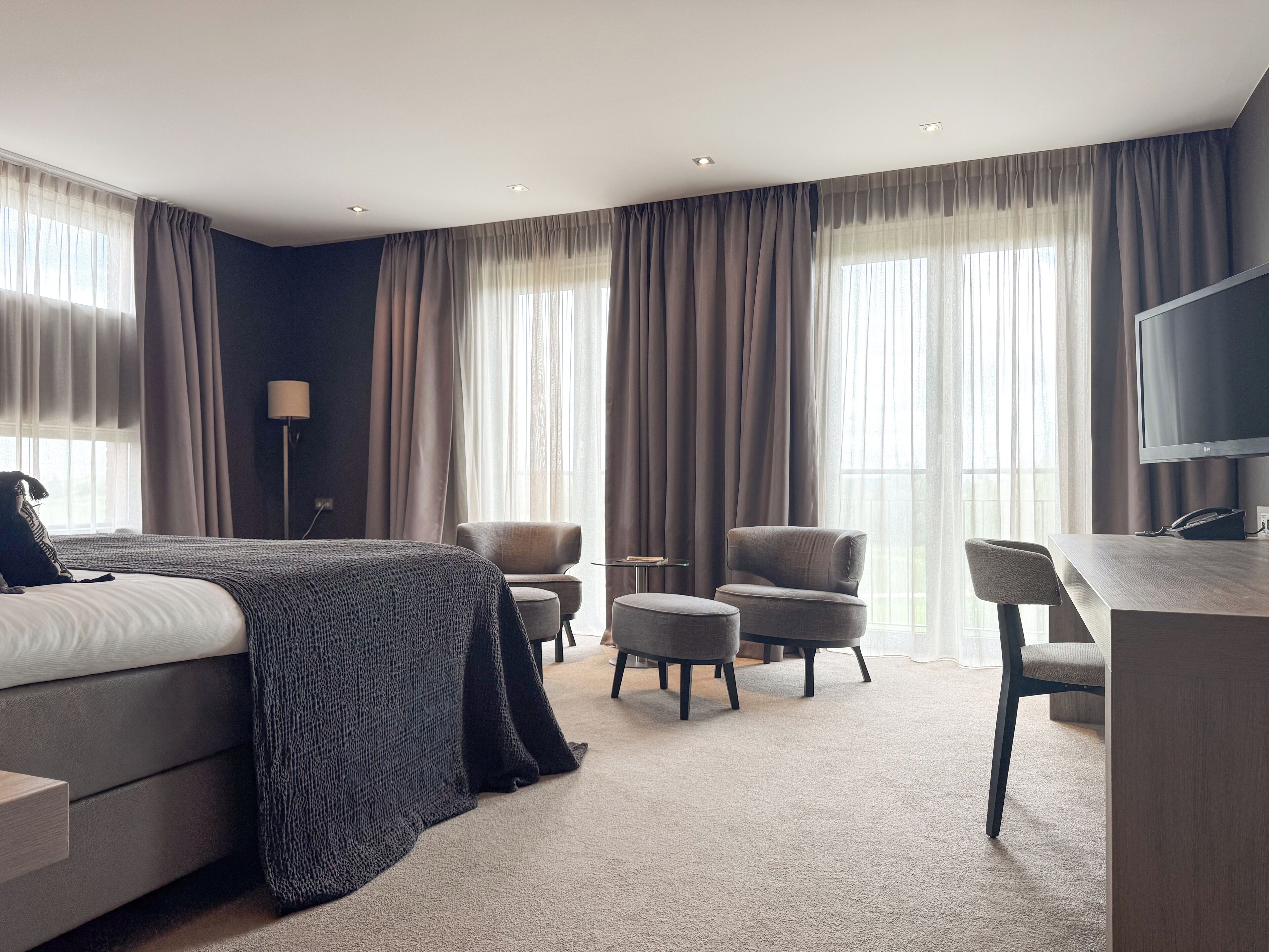 Une chambre d’hôtel moderne avec un grand lit, deux fauteuils, un bureau et une télévision.
