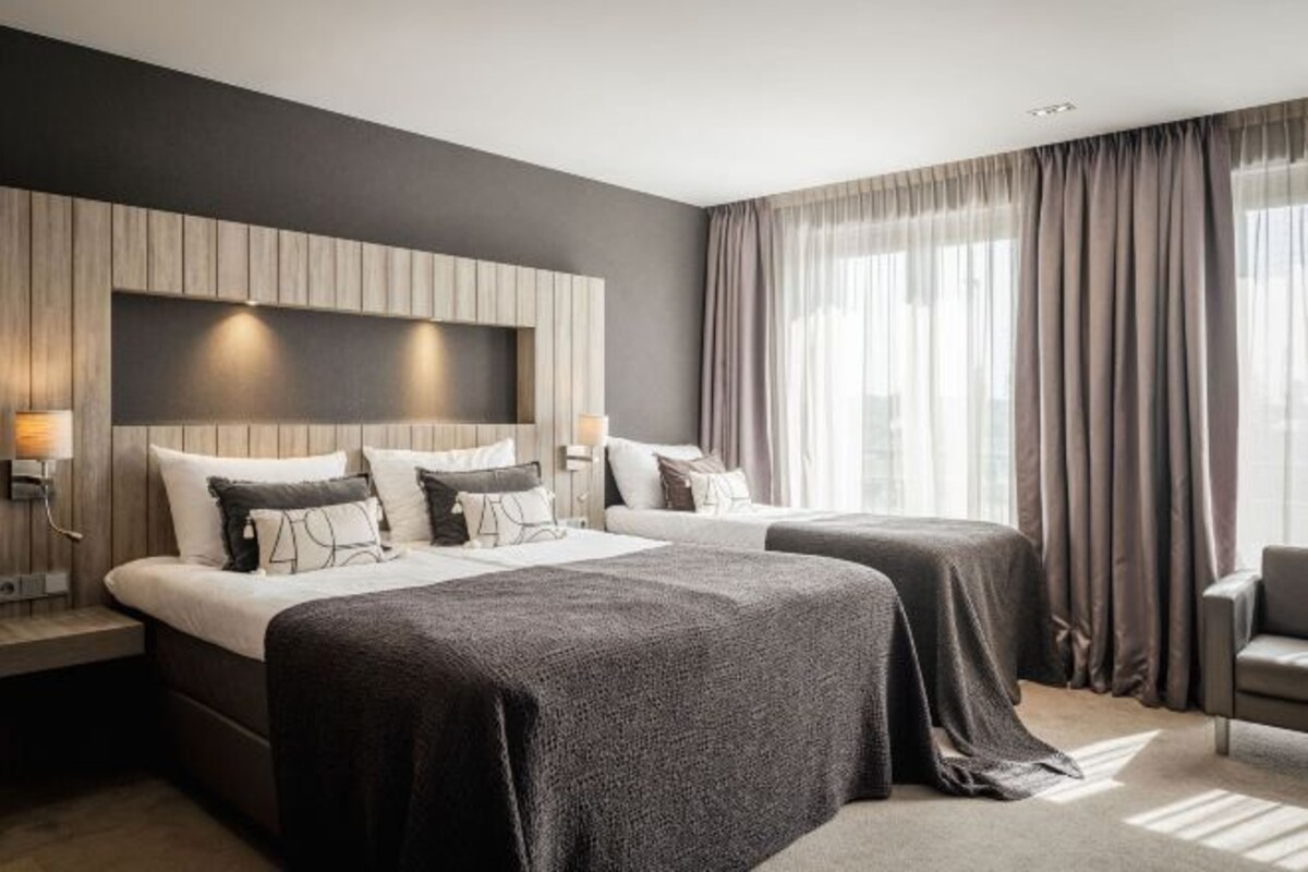 A modern hotel room with two beds, a large wall-mounted TV, and a city view.