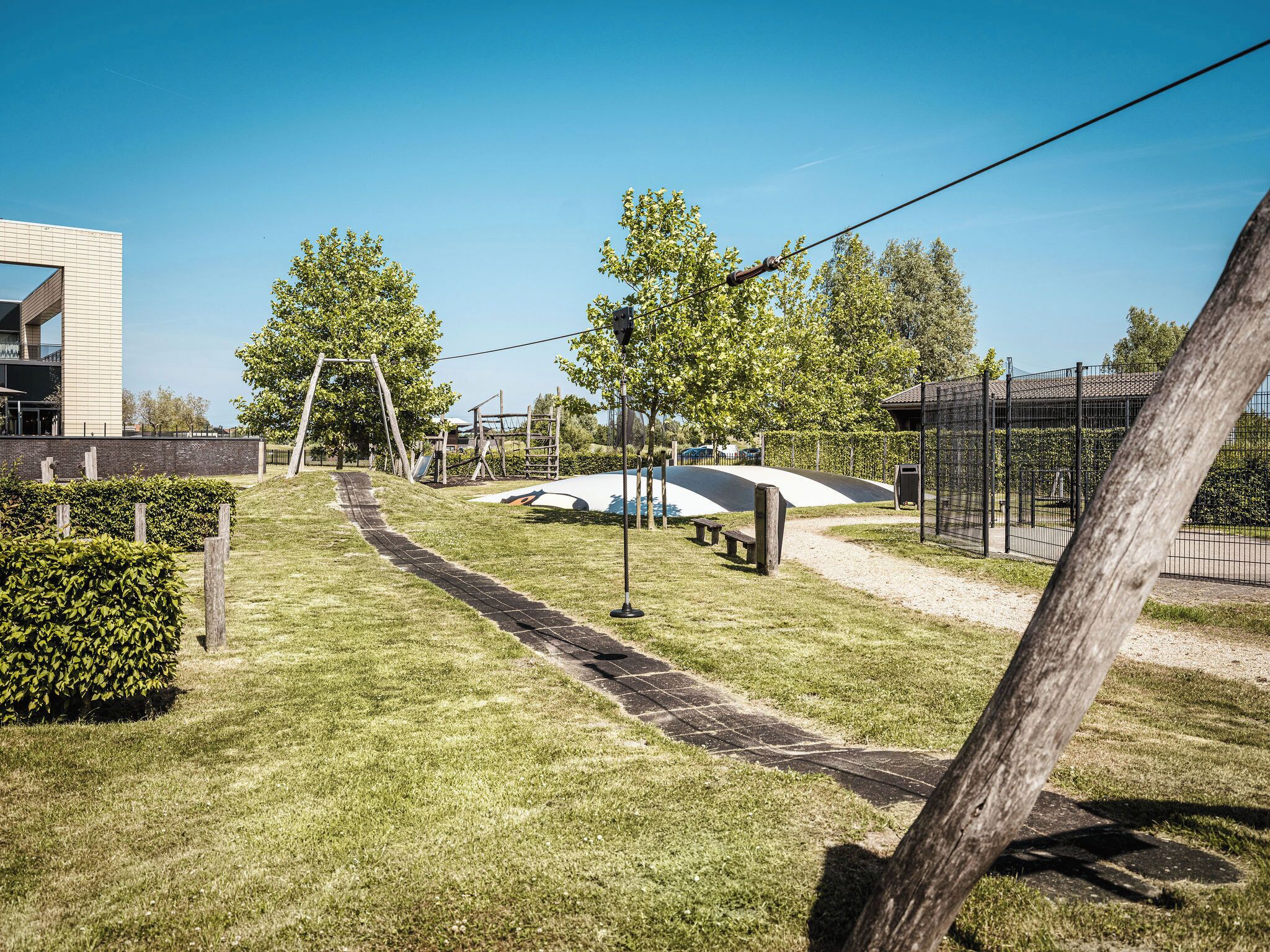 Un área exterior bien cuidada con un parque infantil, un camino pavimentado y un recinto vallado.