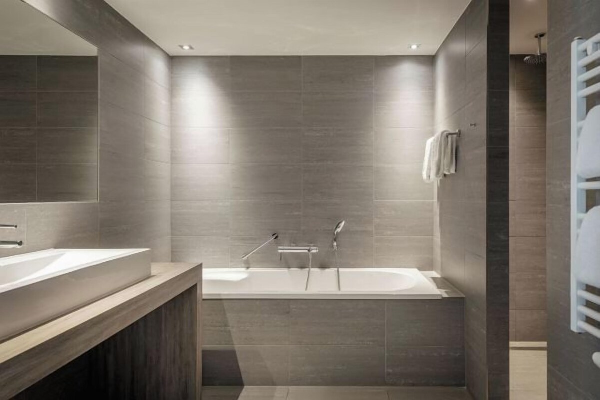 Ein modernes Badezimmer mit einer großen Badewanne, einem Waschtisch inklusive Spiegel und einem Handtuchhalter.