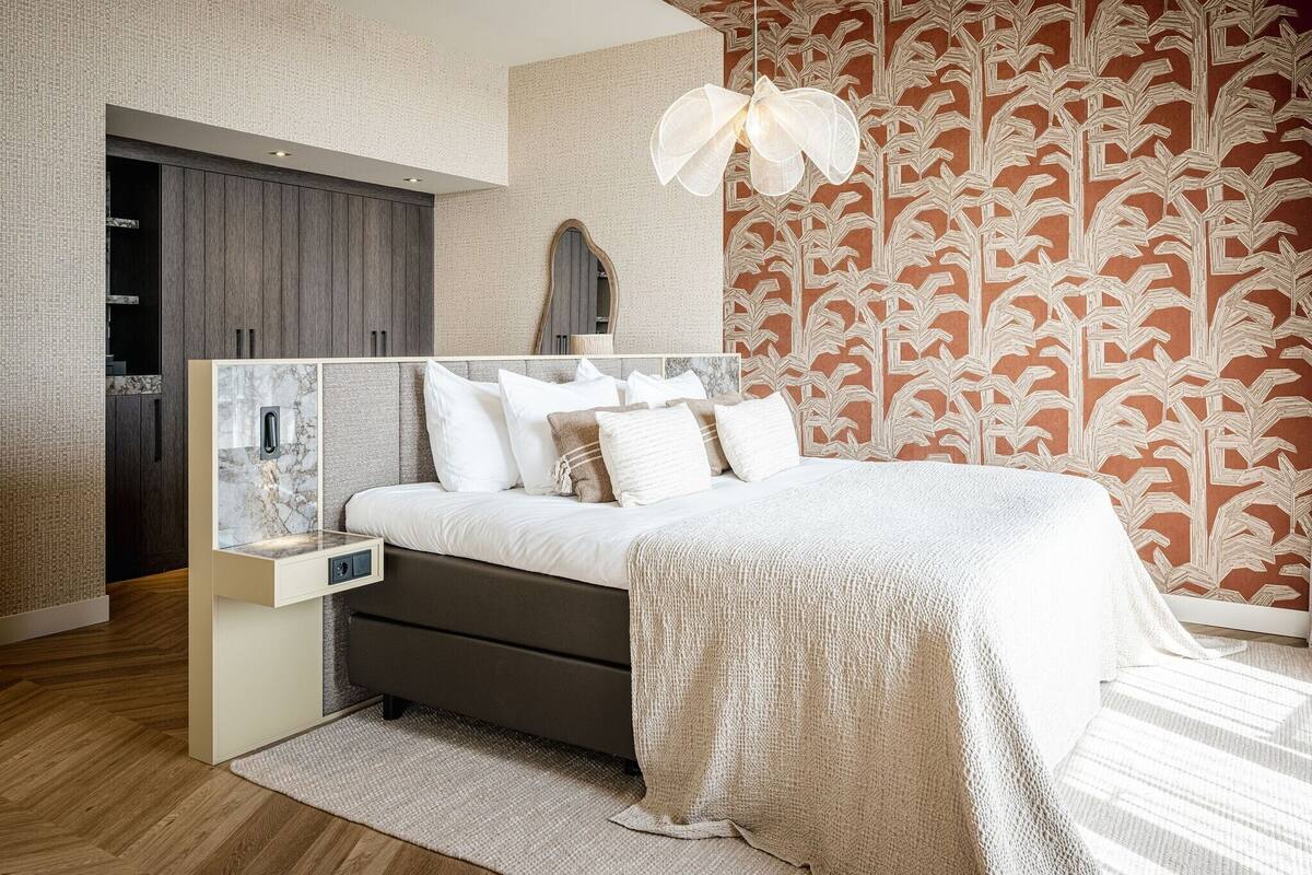 Een moderne slaapkamer met een bed, nachtkastje, kledingkast en behang met patroon.