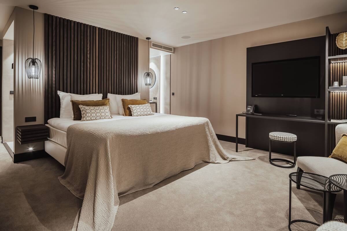 Een moderne slaapkamer met een groot bed, nachtkastjes, een televisie en een zithoek.
