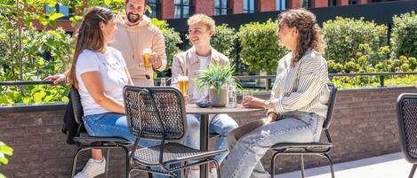 A group of people sitting at an outdoor table with chairs, a potted plant, and a glass of beer.