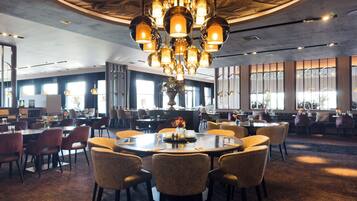 A restaurant with round tables, chairs, and a central chandelier.