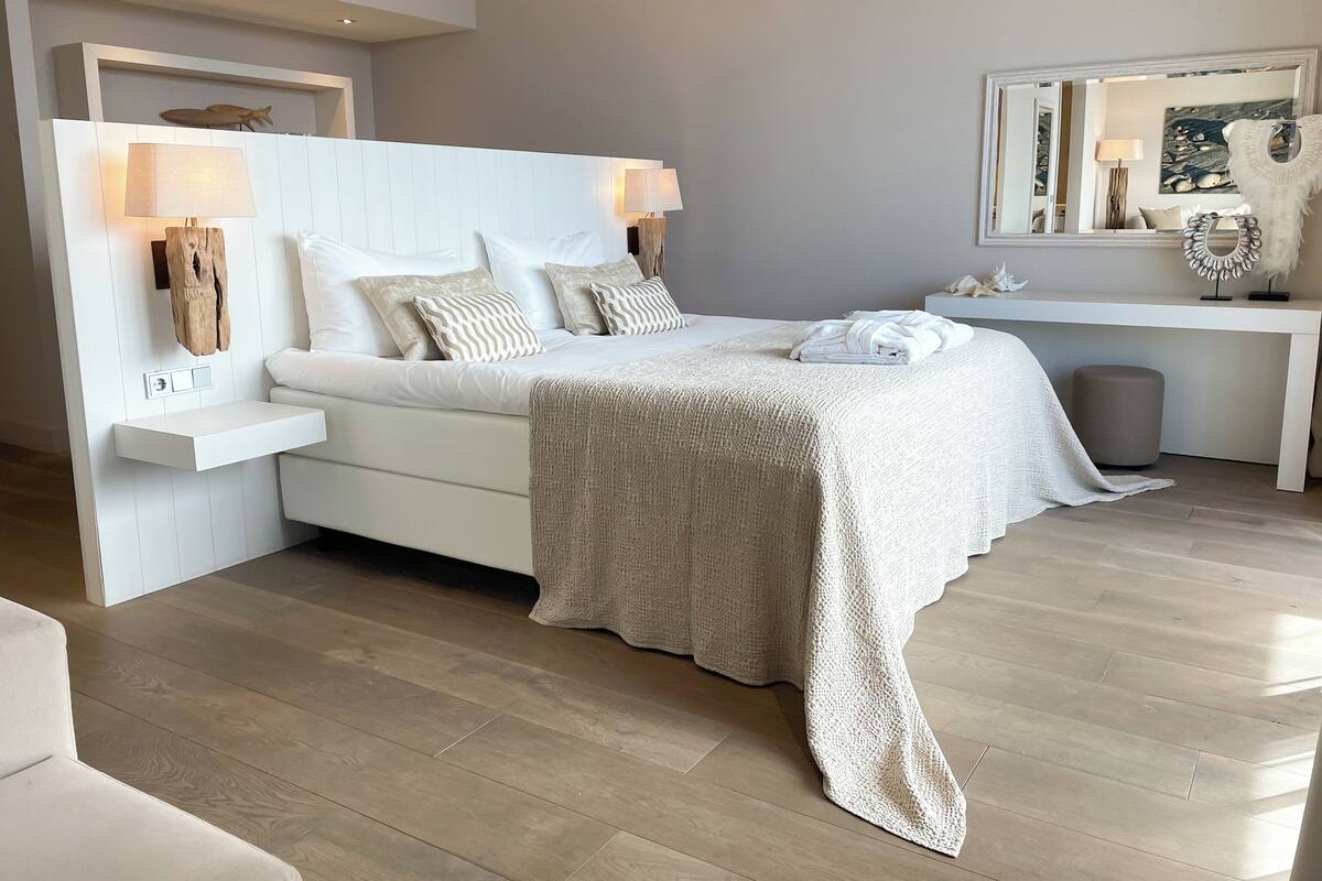 Een moderne slaapkamer met een wit bed, bedlampjes en een grote spiegel.