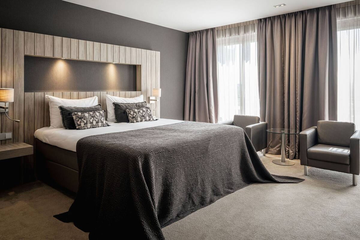 Een moderne hotelkamer met een groot bed, een zithoek met een fauteuil en uitzicht op het omliggende landschap.
