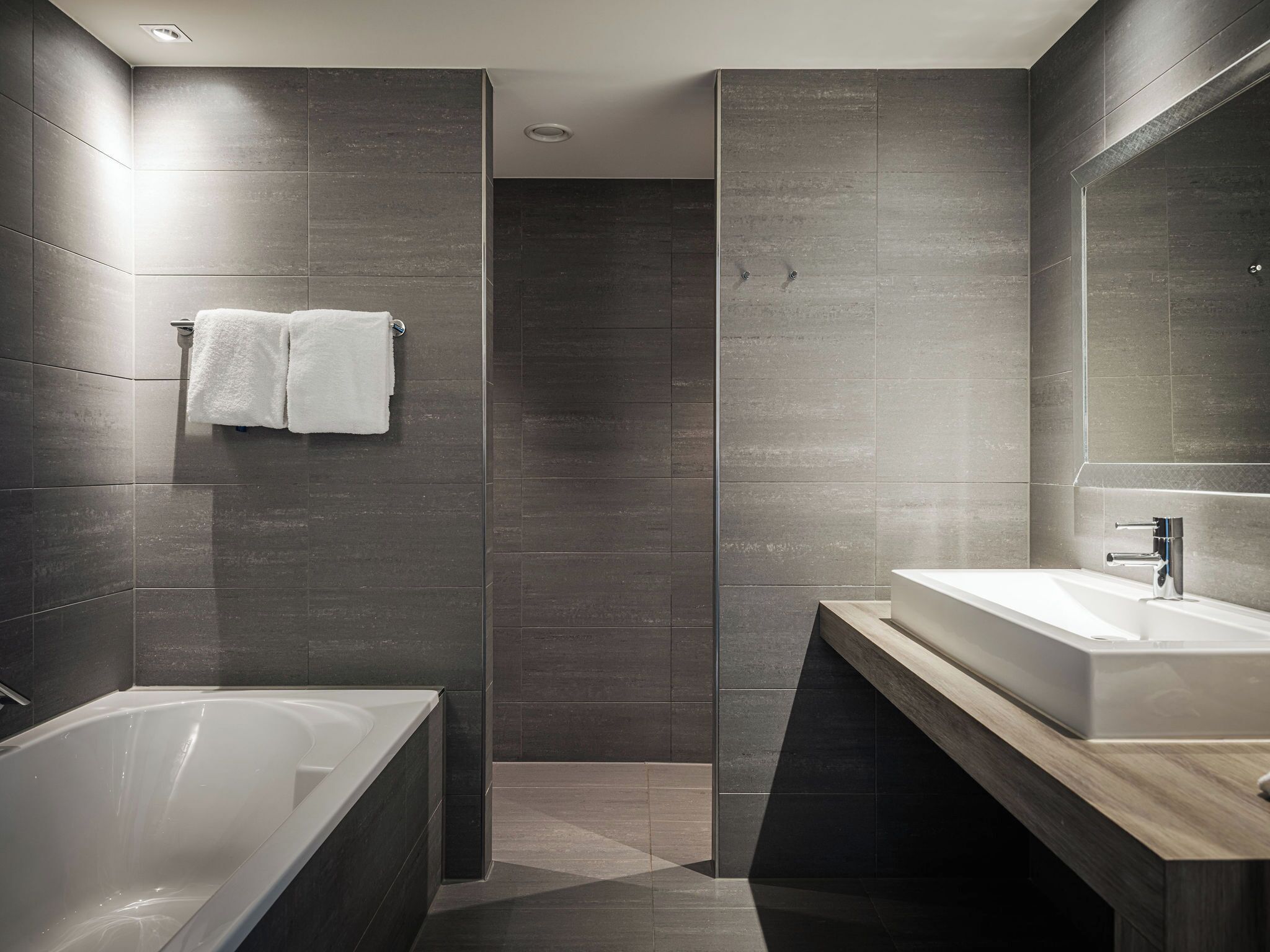Une salle de bain moderne avec des carreaux de couleur foncée, une baignoire, un lavabo et une douche.
