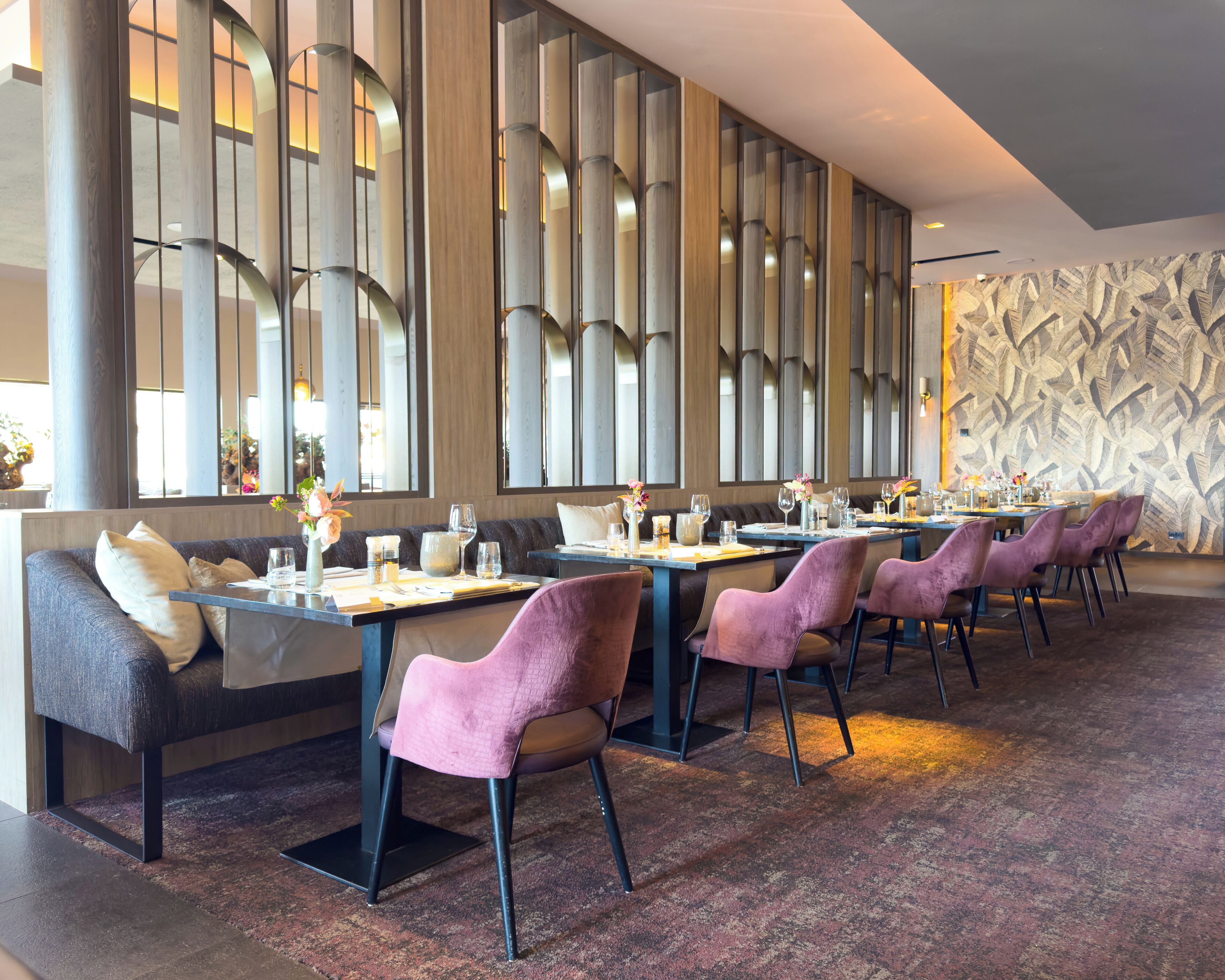 A restaurant with a long table, cushioned seating, and a patterned wall.