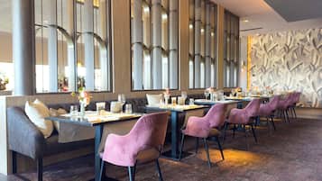 A restaurant with a long table, cushioned seating, and a patterned wall.