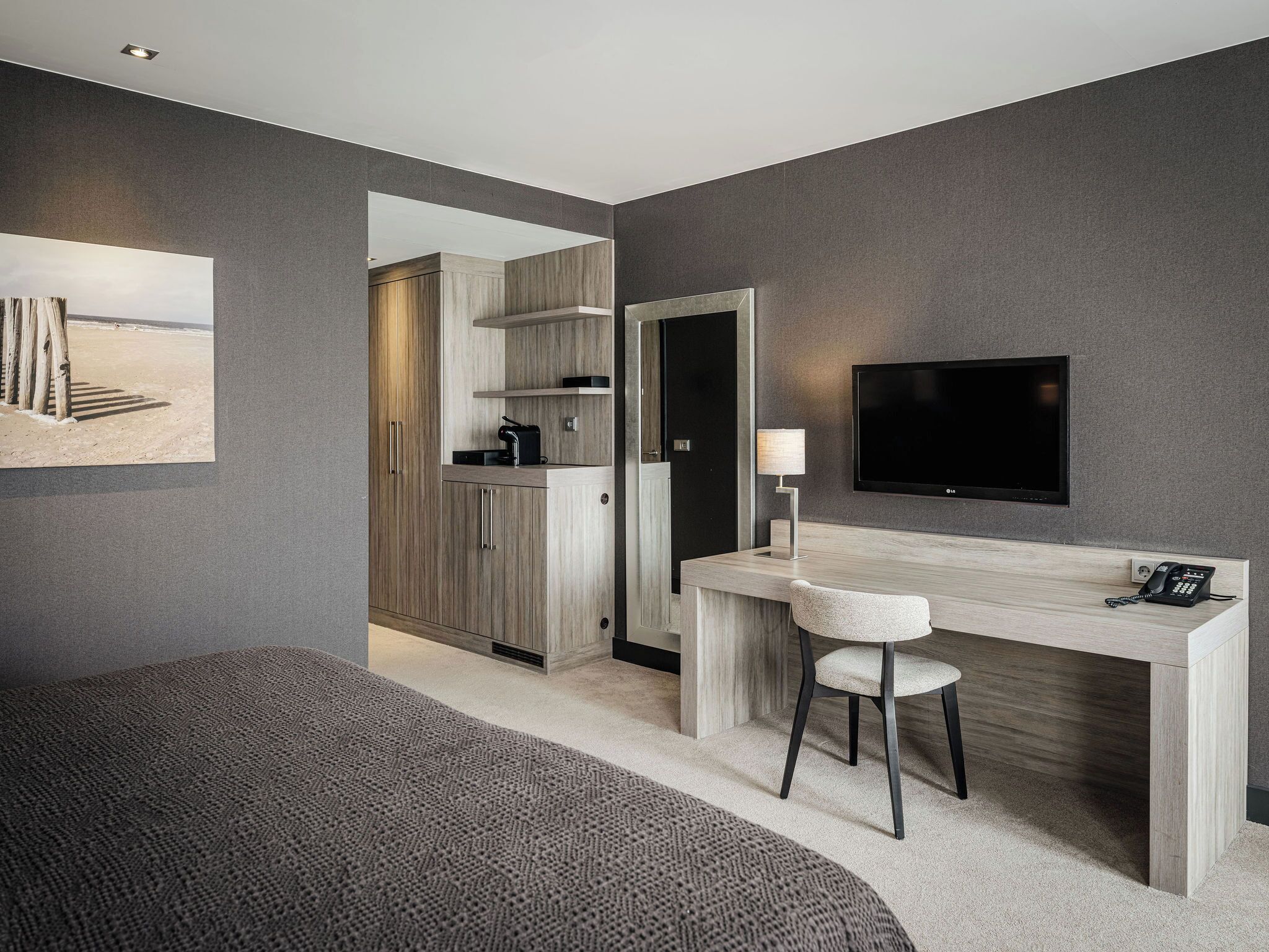 Ein modernes Hotelzimmer mit Bett, Schreibtisch mit Stuhl, Fernseher und einer kleinen Küchenzeile.