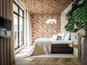 A bedroom with a large window, a bed with a white blanket, a TV mounted on the wall, and a plant. - Van der Valk Hotel Middelburg (Middelburg)