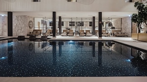 Un espace piscine intérieur moderne, doté de chaises longues et d’une eau cristalline.