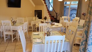 A dining area with white chairs and tables, a staircase, and a view of the outdoors.